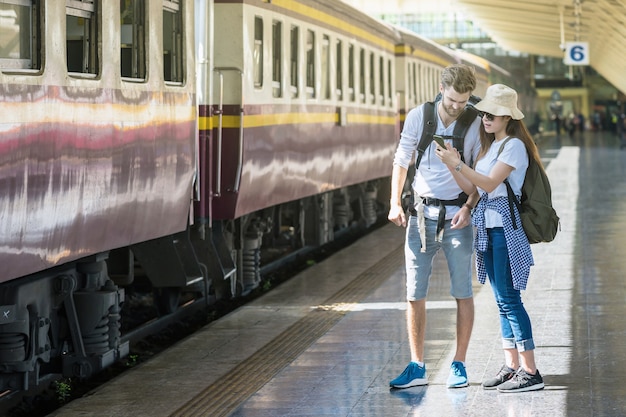 Los viajeros multiétnicos de la pareja están mirando el mapa digital en el teléfono móvil elegante en el stati del tren