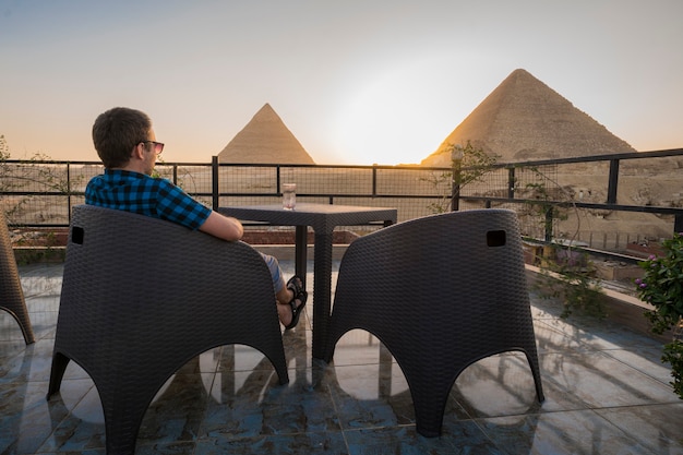 marca llorar Inquieto Viajeros en solitario. un hombre solitario se sienta en la azotea de un  restaurante y disfruta de una hermosa vista de las grandes pirámides de  giza. el cairo, egipto. | Foto Premium