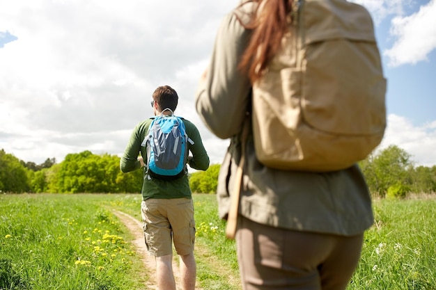 viajes, caminatas, mochileros, turismo y concepto de personas - cerca de una pareja con mochilas caminando por la carretera del campo