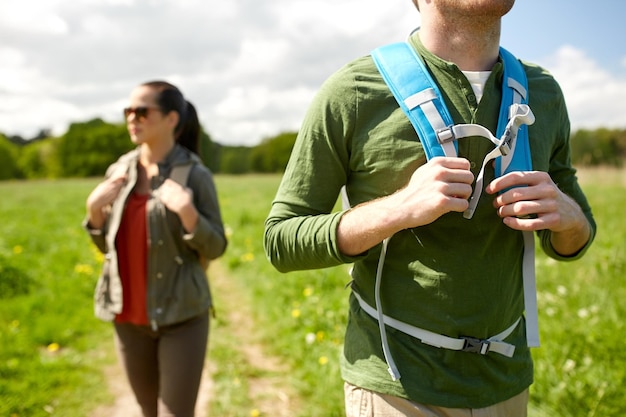 viajes, caminatas, mochileros, turismo y concepto de personas - cerca de una pareja con mochilas caminando por la carretera del campo