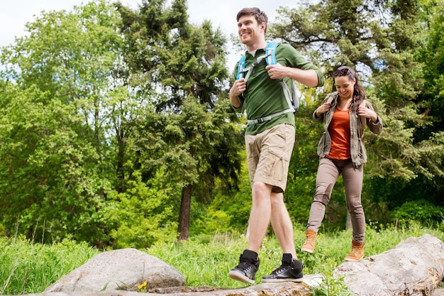 viajes, caminatas, mochileros, turismo y concepto de personas - pareja feliz con mochilas caminando a lo largo del tronco de un árbol caído al aire libre