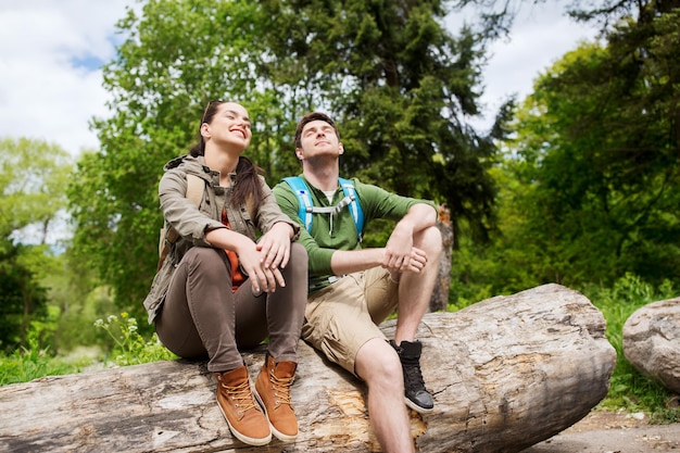 viajes, caminatas, mochileros, turismo y concepto de personas - pareja sonriente con mochilas descansando y disfrutando del sol en la naturaleza