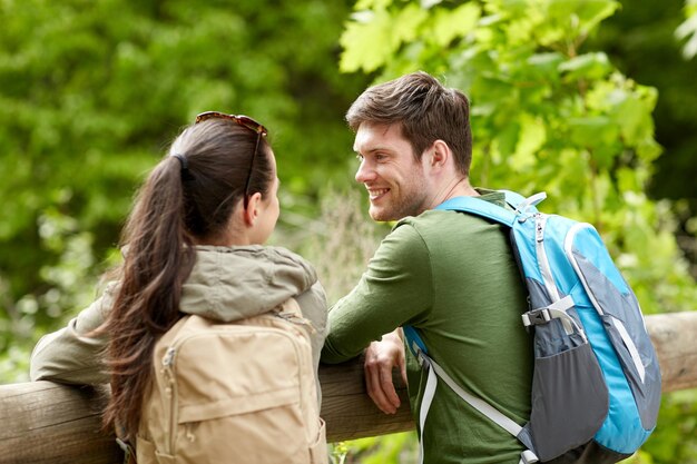 viajes, caminatas, mochileros, turismo y concepto de personas - pareja sonriente con mochilas en la naturaleza mirando y hablando entre ellos