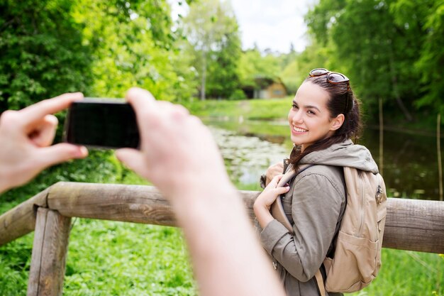 viajes, caminatas, mochileros, turismo y concepto de personas - pareja sonriente con mochilas tomando fotos por teléfono inteligente en la naturaleza