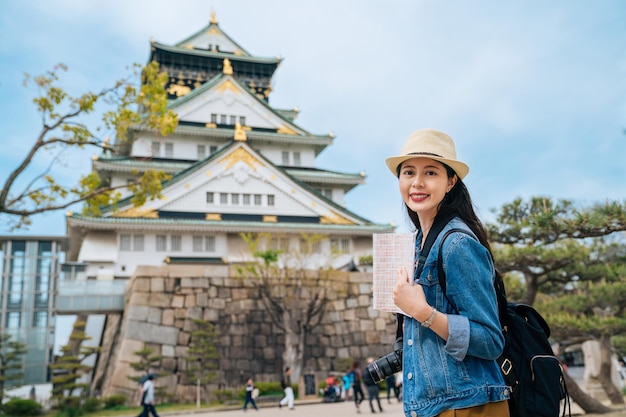 viajes independientes en el concepto de estilo de vida de Japón. mujer viajera sosteniendo una guía visitando el castillo de osaka sola con mochila y cámara slr. cámara de cara de chica joven sonriendo alegremente.