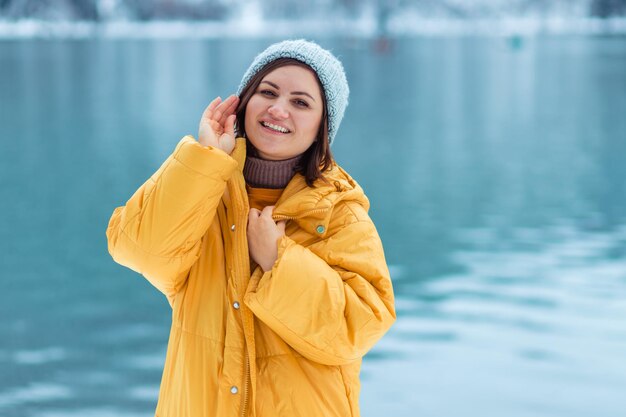 Foto viajes de invierno por europa. retrato de una hermosa joven con una chaqueta amarilla en la orilla de un lago alpino en invierno. vista del lago alpino con nieve.