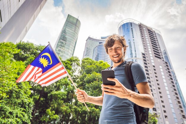 Viajes y tecnología Joven turista con la bandera de Malasia está mirando un mapa de la ciudad en un teléfono inteligente para navegar