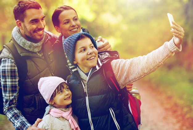 viajes, turismo, senderismo, tecnología y gente concepto - familia feliz con mochilas tomando selfies con teléfonos inteligentes en el bosque