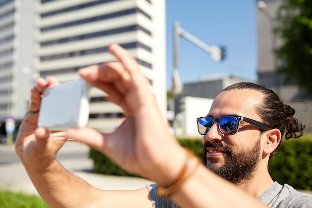 viajes, turismo, tecnología y concepto de personas - hombre sonriente tomando video o selfie por teléfono inteligente en la calle de la ciudad de verano