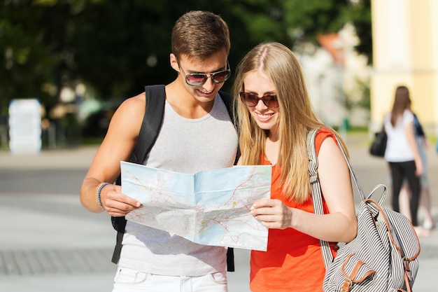 viajes, turismo, vacaciones de verano y concepto de personas - pareja sonriente con mapa y mochila buscando ubicación en la ciudad