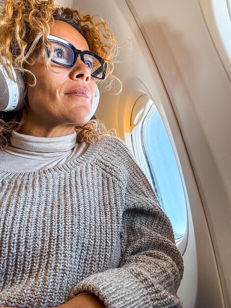 Viajes y vacaciones Mujer atractiva de mediana edad escucha música y se relaja sentada en un cómodo asiento de avión