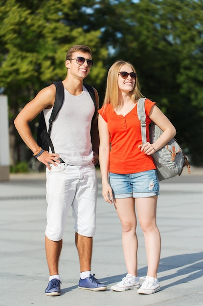 viajes, vacaciones de verano, turismo y concepto de amistad - pareja sonriente con mochilas en la ciudad