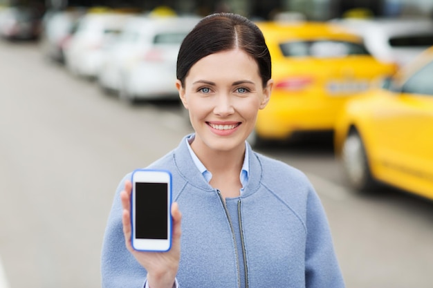 viajes, viajes de negocios, personas y concepto de turismo - mujer joven sonriente que muestra la pantalla en blanco del teléfono inteligente sobre la estación de taxis o la calle de la ciudad