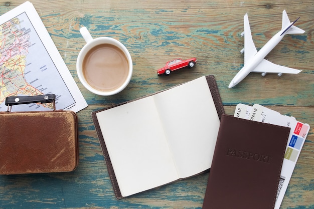 Viajes, viajes de vacaciones, turismo - cierre cuaderno, maleta, avión de juguete y mapa turístico en mesa de madera.