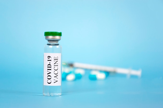 Vial de una sola botella de vacuna Coronavirus COVID-19, píldoras y jeringa sobre fondo azul.