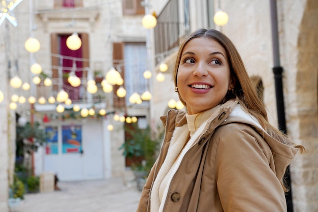 Vibrações natalinas Aproximação de mulheres de inverno caminhando entre becos decorados com luzes na cidade histórica à noite