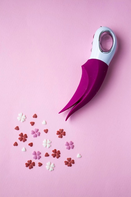 Vibrador rosa com um brinquedo de alça branca para adultos encontra-se em um fundo rosa perto dos corações decorativos imitando um orgasmo foto conceitual