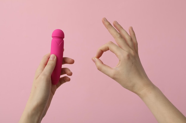 Vibrador rosa en manos sobre fondo rosa gesto ok