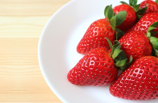 Vibrierende rote frische reife Erdbeeren ausgerichtet auf einer weißen Platte auf Holztisch