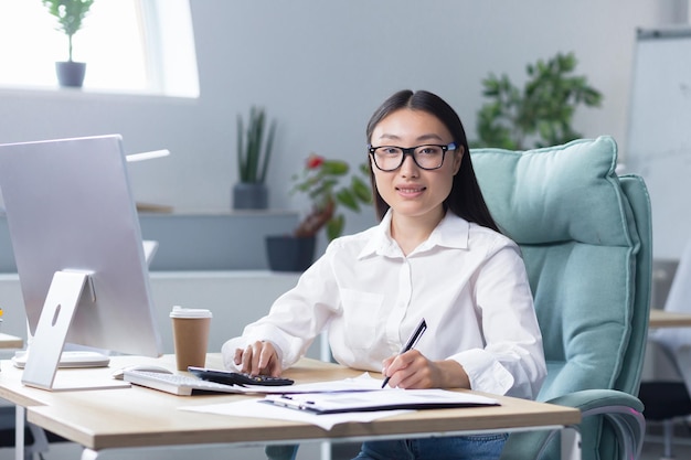 Viciada em trabalho, uma jovem empresária asiática sentada à mesa bebendo café para tomar um copo de papel de