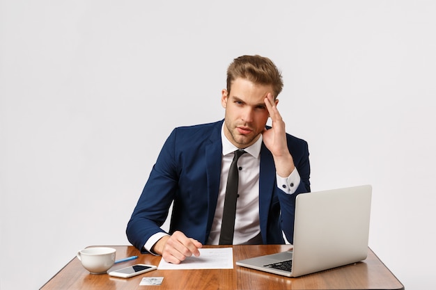 Viciado em trabalho jovem sério e cansado, empresário no escritório, sentindo-se tonto e angustiado, trabalhando o dia todo, sentado com laptop, documentos e café, tocando o templo, com dor de cabeça