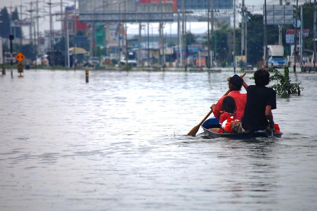 Las víctimas de desastres naturales de los tailandeses usan embarcaciones que se meten en el agua en la calle del callejón mientras el camino de la inundación del agua espera ayuda para el rescate y las donaciones en el campo rural en Nonthaburi Tailandia
