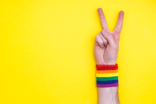 Victory-Handgeste mit Gay-Pride-Regenbogenfahnen-Armband auf gelbem Hintergrund