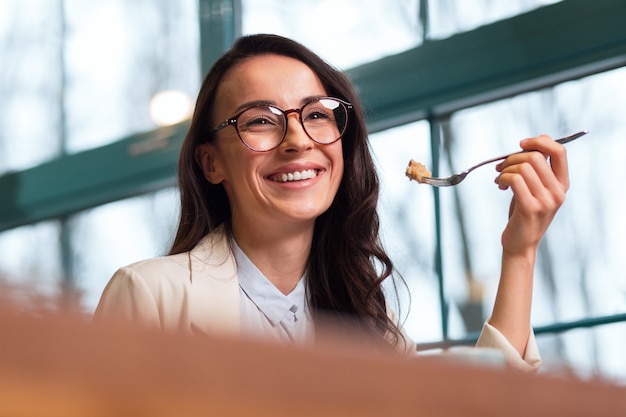 Vida boa. Mulher simpática e atraente, alegre, comendo enquanto pega um garfo e rindo