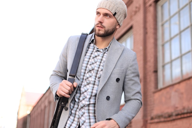 Vida en la ciudad. Hombre joven con estilo en abrigo gris y sombrero caminando por la calle en la ciudad.