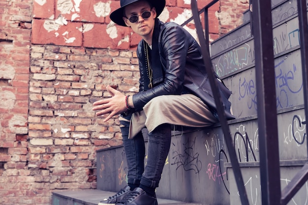 Foto vida en la ciudad. hombre joven con estilo en traje de moda está sentado en las escaleras