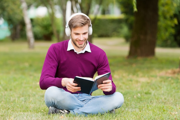 Vida de estudante. educação com ebook. homem sorridente no fone de ouvido, ouvindo música enquanto lia o livro. cara abre o caderno para fazer anotações. obter informações úteis. homem gosta de ler.