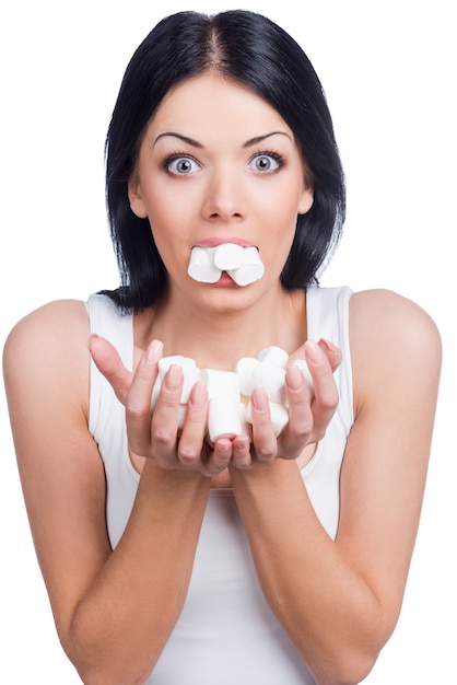 Vida doce. Mulheres bonitas segurando marshmallow na boca e nas mãos em pé contra um fundo branco