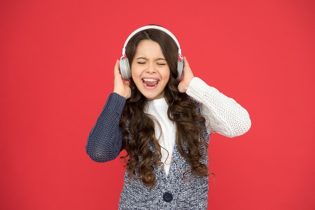 La vida es canción, cántala. Niño feliz canta fondo rojo de la canción. Niña escucha la canción en auriculares. Vida moderna. Nueva tecnología. Música y canto. Diversión y entretenimiento.