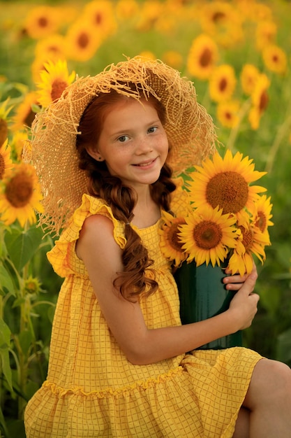 Vida feliz no retrato de verão de uma linda garota ruiva com um chapéu em um campo de girassóis com flores nas mãos nos raios do sol poente