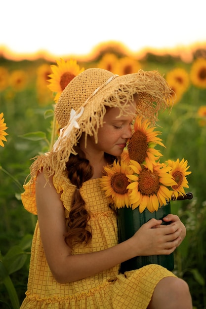 Vida feliz no retrato de verão de uma linda garota ruiva com um chapéu em um campo de girassóis com flores nas mãos nos raios do sol poente