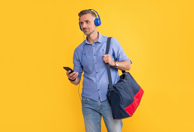 La vida moderna y el estilo de vida chico chateando en auriculares hombre de negocios sonriente en auriculares usar teléfono inteligente con bolsa de viaje hombre escuchar música y sostener bolsa de deportes