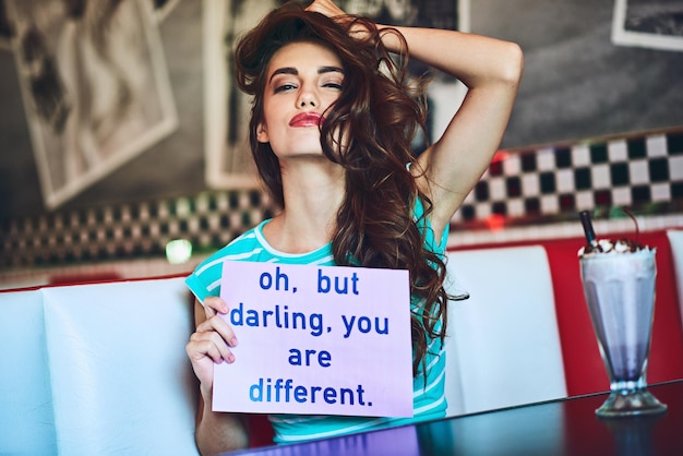 Foto la vida no sería divertida si todos fuéramos iguales retrato recortado de una atractiva joven sosteniendo un cartel mientras disfruta de un batido en un restaurante retro