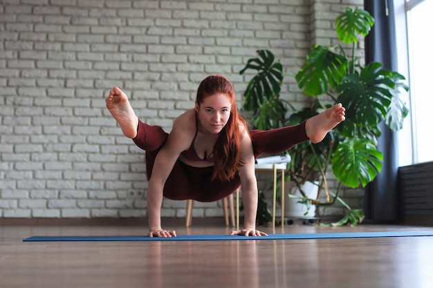 Vida saludable. Mujer atractiva practicando yoga en casa, haciendo ejercicio, vistiendo ropa deportiva.