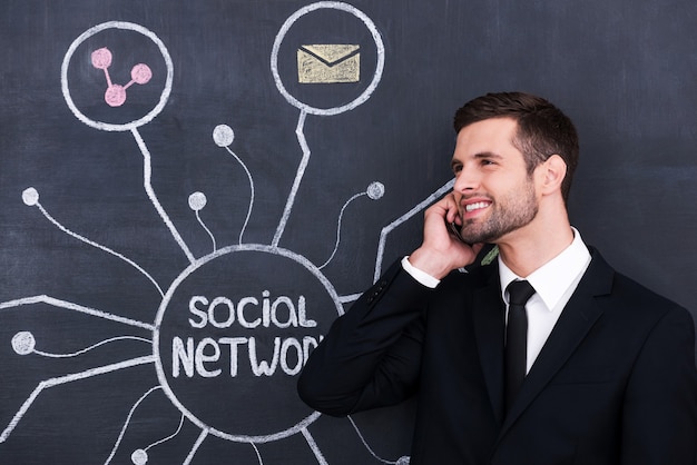 Vida social ativa. jovem bonito falando ao telefone em pé contra uma rede social, desenhando na lousa