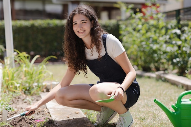 Foto vida suburbana joven mujer sonriente con cabello rizado trabajando en el jardín plantando flores en un suelo fructífero en el jardín