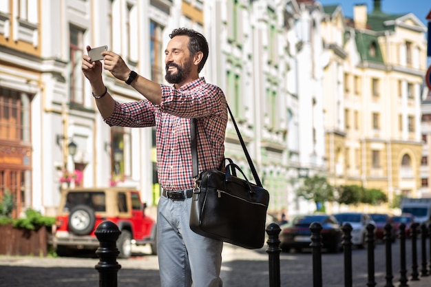 Foto vida urbana. homem alegre e encantado parado na rua enquanto tira fotos