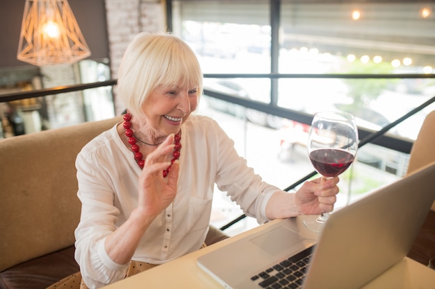 Video chamada. Mulher idosa elegante tomando um pouco de vinho e conversando por vídeo