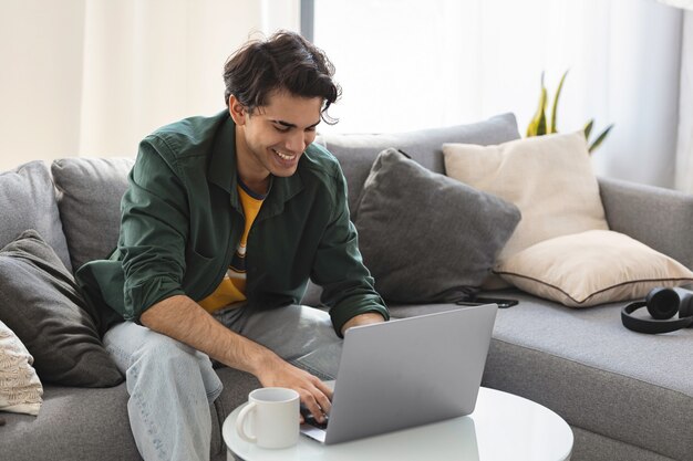 Videoanruf. Der junge tausendjährige Kaukasier kommuniziert in sozialen Netzwerken oder arbeitet online mit einem Laptop, der zu Hause auf der Couch sitzt