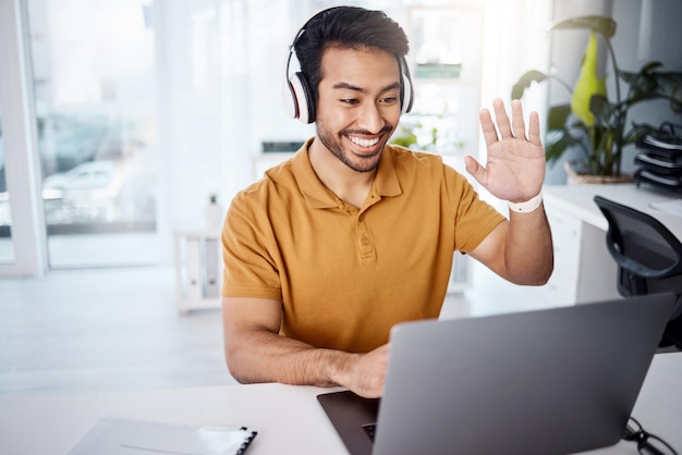 Foto videoanrufcomputer und kopfhörer eines mannes, der vom heimbüro aus für ein webinar oder ein virtuelles online-meeting arbeitet und spricht. glückliche asiatische person winkt auf seinem laptop oder pc im kundenchat für unternehmen hallo