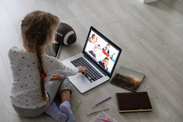 Una videoconferencia de niña con feliz maestra en portátil