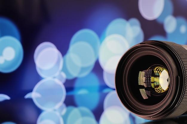 Videografista e fotógrafo de equipamentos. Lentes em cima da mesa no contexto de lâmpadas brilhantes. Brilho e bokeh no reflexo do vidro da câmera.