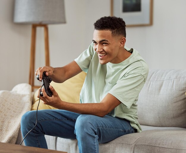 Foto videojuegos de hombre feliz y jugando en el sofá con el controlador en la sala de estar para divertirse en línea en casa joven hombre disfrutando del tiempo de juego en la consola para una competencia amistosa o deportes electrónicos en casa