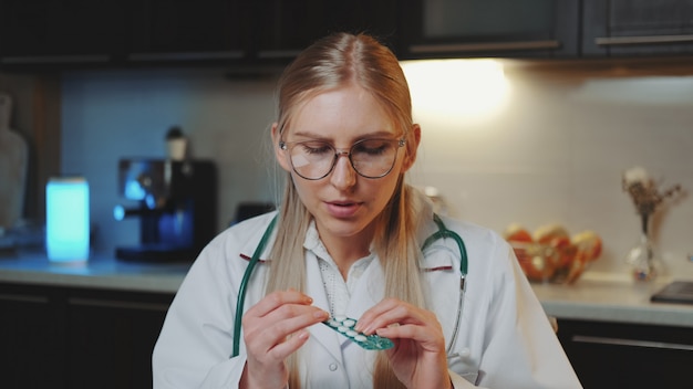 Videollamada al paciente: doctora en bata médica mirando a la cámara y explicando cómo tomar medicamentos