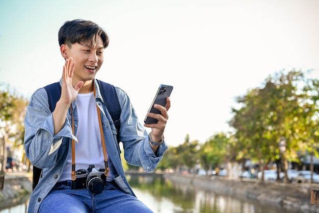 Videollamada de un viajero asiático con su amigo a través de un teléfono inteligente mientras pasea por la ciudad