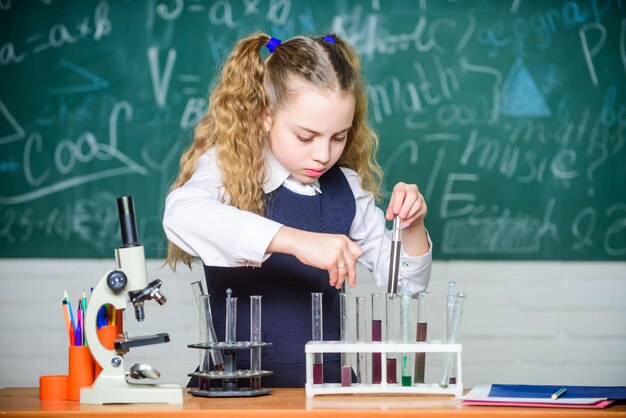 Vidraria de laboratório Futuro microbiologista Laboratório escolar Garota inteligente estudante conduz experimento escolar Aluno escolar estuda líquidos químicos Lição de química escolar Tubos de ensaio com substâncias
